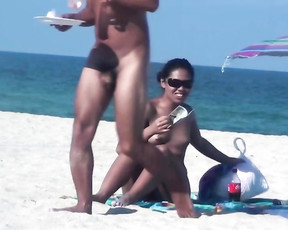 Young babe in nudist colony is eating on the sandy beach